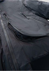 Zwarte donzen jas met een gladde buitenlaag, opvallende ritsen en met gaas gevoerde zakken, met een zachte geribbelde stof aan de onderkant.