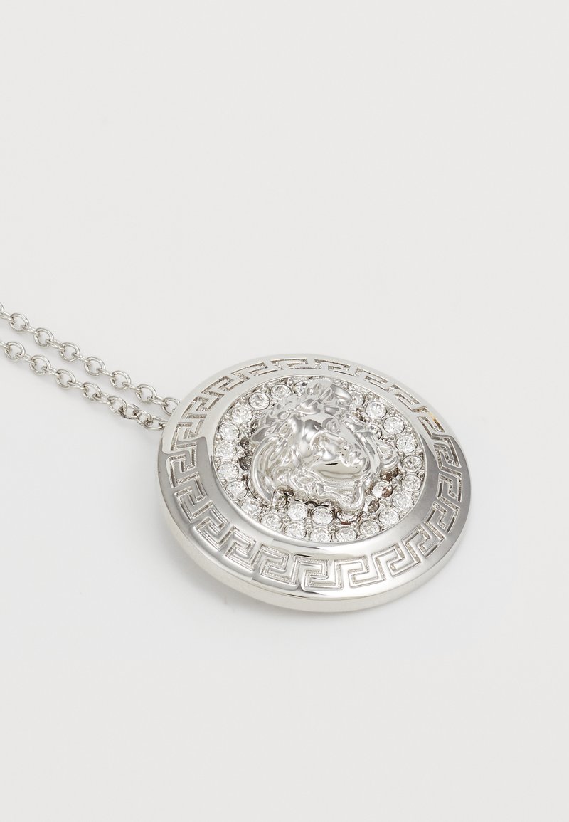 Silberne Anhängerkette mit einem Löwenkopfdesign, umgeben von einer kreisförmigen Anordnung von Strasssteinen und einem geometrisch gemusterten Rand.