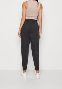 Mustat hikipaidat elastisilla haitoilla, yhdistettynä beigeen ilmanhihaiseseen paitaan, jossa on avainaukko takana. Yksinkertainen tausta.