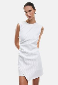 Abito bianco a tinta unita con righe verticali, design senza maniche e orlo asimmetrico. Realizzato in tessuto liscio con una leggera lucentezza.