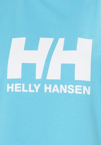 Světle modré bavlněné tričko se velkým bílým logem "HH" a textem "HELLY HANSEN" tištěným pod ním v tučném, velkém písmu.