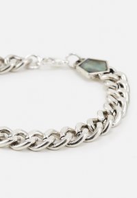 Pulseira de corrente em prata com elos interligados, acabamento polido e um detalhe hexagonal no fecho.