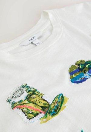 White cotton t-shirt featuring colorful embroidered patches of pickles and jars, with accents of green, blue, and red thread detail.