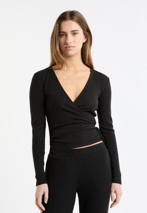 Top nero a maniche lunghe con coste, scollo a V profondo e design a incrocio. Realizzato in tessuto strutturato, ha una silhouette aderente e un orlo corto.