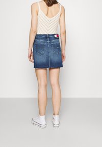 Denim mini kjol med en blekt mörkblå tvätt, fransad nederkant och två bakfickor. Bärs med en ljusstickad tanktop och vita sneakers.