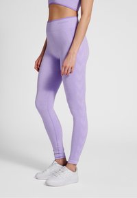 Fioletowe legginsy wykonane z elastycznego materiału z teksturowanym wzorem. Wysoki stan, w zestawie z białymi sneakersami.