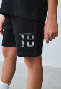Sorte shorts lavet af bomuldsblanding med en tætsiddende pasform. Har et hvidstribet logo "B" på venstre ben. Ubehandlede kanter.