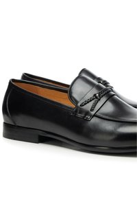 Schwarze Leder-Loafer mit glatter Oberfläche, verziert mit einer dekorativen, geflochtenen Schnürung und einem niedrigen, geschichteten Absatz. Klassisches Design.