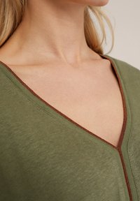 Top de color verde oliva con un diseño de escote en V y un ribete en marrón que contrasta. Textura suave y líneas simples y limpias.