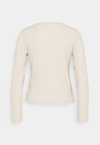 Haut à manches longues côtelé en beige clair. Encolure ronde, structure ajustée, texture douce et design minimaliste. Pas de motifs ni d'accents visibles.