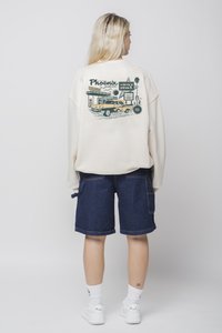 Σακάκι crewneck σε κρεμ απόχρωση με μια vintage γραφική παράσταση ενός πρατηρίου καυσίμων και ενός αυτοκινήτου στην πλάτη. Συνδυάζεται με μπλε τζιν σορτς.
