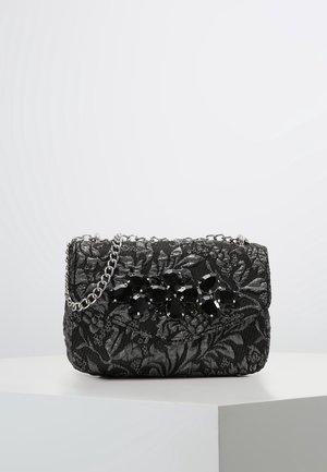 Schwarze strukturierte Clutch mit floralem Spitzenmuster, schwarzer floraler Edelsteinverzierung und silberner Kette, die auf einer weißen Oberfläche liegt.