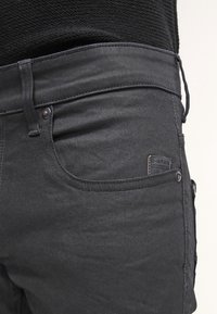 Jeans de mezclilla negra con un diseño de cinco bolsillos, herrajes en plata y un parche de cuero de la marca en el bolsillo frontal. Tejido texturado con un ligero estiramiento.