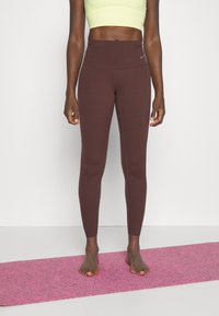 Brązowe legginsy z wysokim stanem wykonane z elastycznego materiału, charakteryzujące się gładkim wykończeniem i subtelnym logo Nike, w połączeniu z neonowożółtą crop top.