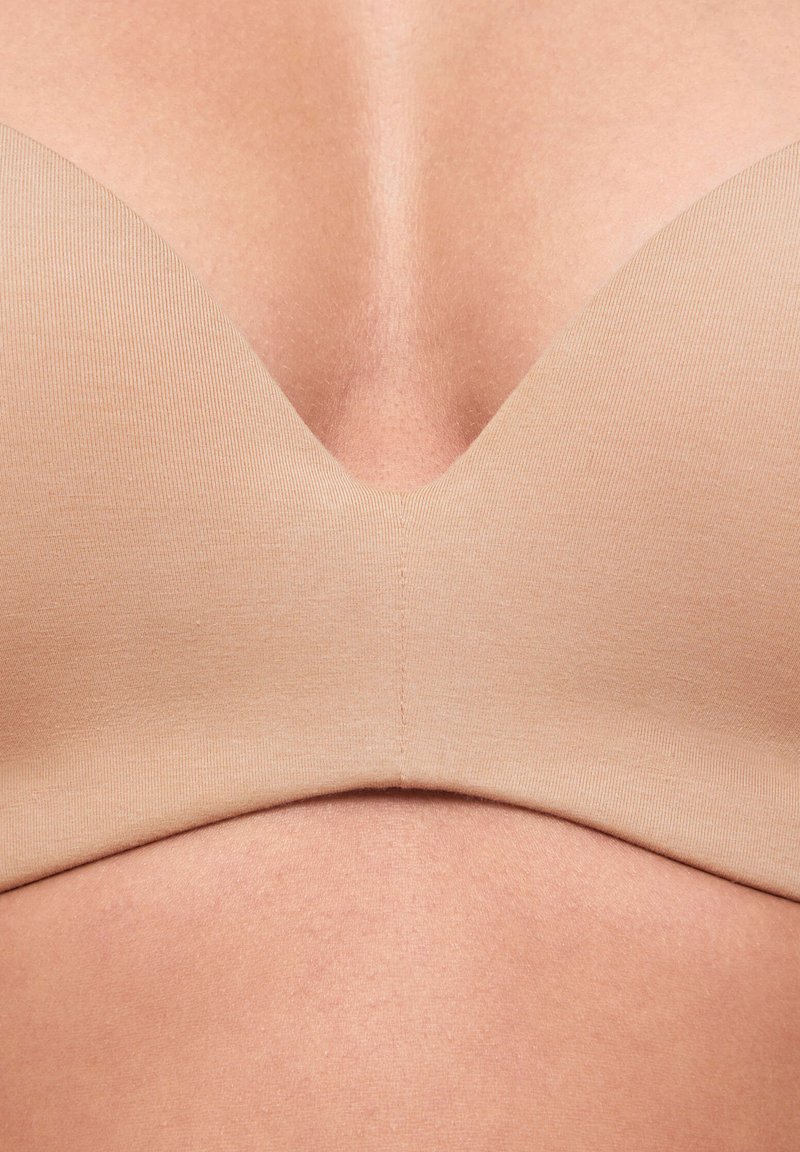 Gros plan sur la poitrine d'une personne portant un soutien-gorge beige lisse et sans coutures avec un décolleté en V plongeant.