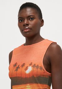 Top de tanque naranja con un estampado gráfico de atardecer y palmera. Tejido suave con un corte holgado y diseño sin mangas.