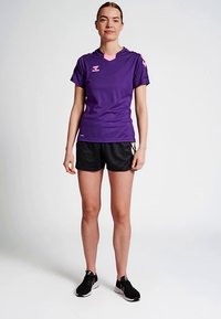 Camisola atlética roxa de manga curta com decote em v e detalhes cor-de-rosa, combinada com calções pretos e ténis pretos, concebida para atividades desportivas.