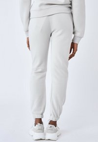 Pantalones de chándal gris claro de tela suave con puños elásticos. La parte trasera presenta un diseño liso, complementado por deportivas blancas deportivas.