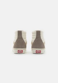 Zapatillas altas de ante y lienzo beige, con un cuello acolchado, suela de goma blanca y etiqueta de logo roja en la parte trasera.