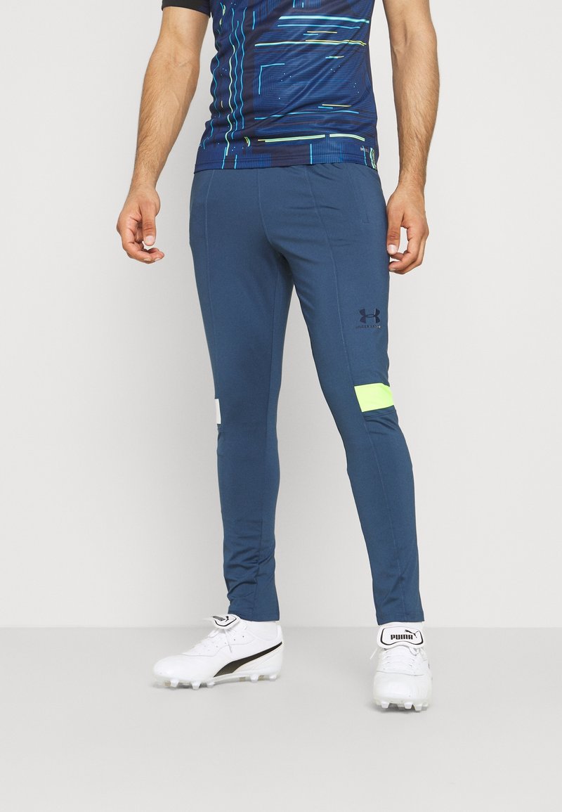 Pantalones deportivos azul marino con un ajuste ceñido, con un detalle en verde neón y el logo de Under Armour en el muslo. Tejido suave y elástico.
