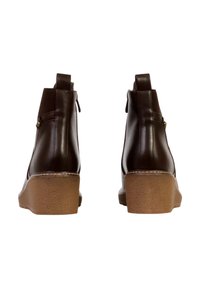 Bottines en cuir marron à finition lisse, dotées d'une semelle compensée, d'une fermeture éclair à l'arrière et d'accents de boutons décoratifs sur le côté.