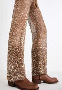 Bronze sequined pants with a loose fit, featuring a textured surface and wide legs, paired with brown ankle boots with a low heel.