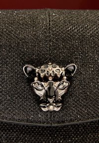 Pochette nera testurizzata con un vistoso fermaglio a forma di testa di pantera nera adornato con strass trasparenti. Dettagli della superficie scintillanti in evidenza.