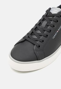 Czarne syntetyczne sneakersy o gładkiej fakturze, złożonym wzorze sznurowania, perforowanymi akcentami i kontrastującą białą podeszwą.