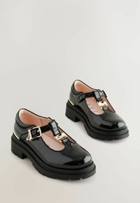 Černé lakované T-bar boty s akcenty ze zlatého kovu, kulatou špičkou, robustní podrážkou a jemným růžovým vnitřkem. Odolný a elegantní design.