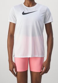 Vit atletisk t-shirt med svart Nike-logga, med en gradientdesign som övergår till rosa, i kombination med klara rosa tajta shorts.
