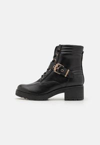 Botas negras hasta el tobillo de cuero sintético, con un tacón robusto, parte delantera con cordones, hebilla lateral y panel trasero texturizado.