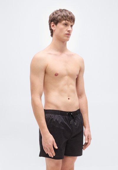 Μαύρο μαγιό σορτς με υφή και κορδόνι στη μέση, με άνετη εφαρμογή και ελαφρύ υλικό, παρουσιασμένο σε μοντέλο.