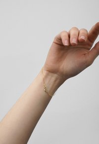 Gold chain bracelet on a wrist, featuring small circular accents and a delicate design, resting against a light background.