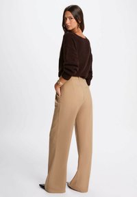 Maglione marrone a maglia con vestibilità ampia e maniche larghe, abbinato a pantaloni beige a vita alta e gamba dritta e tacchi neri.
