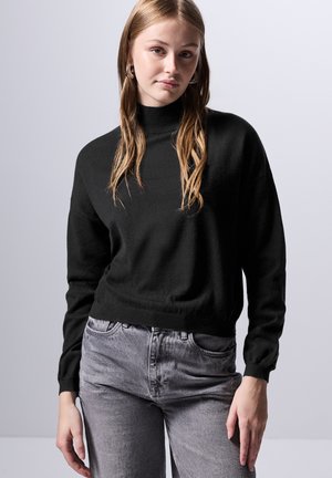 Czarny, teksturowany sweter z golfem i długimi rękawami, zestawiony z jasnoszarymi, wysokim stanem dżinsami. Prosty, casualowy design bez wzorów.