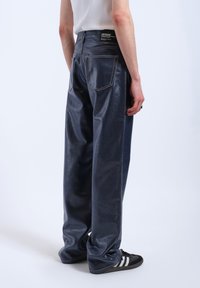 Dark blue denim trousers with a loose fit, featuring contrasting stitching and two back pockets. Elastic waistband with brand tag visible.