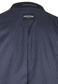 Schwarze Jacke mit geometrischem Muster, ausgestattet mit einem Logo-Label auf der Rückseite, gefertigt aus einem glatten Stoff mit einem dezenten Glanz.