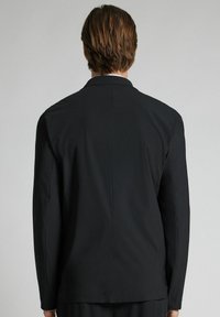 Svart blazer med skräddarsydd passform, utrustad med slagkrage, långa ärmar och slät tyg. Bakdelen visar en mittsöm.