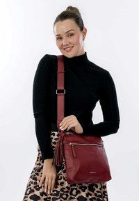 Red leather crossbody bag with a textured finish, adjustable strap, and zipper pocket. Accented with a tassel detail.