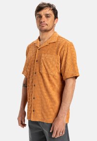 Short-sleeve shirt in textured burnt orange fabric with an embossed pattern, featuring a chest pocket and front buttons.