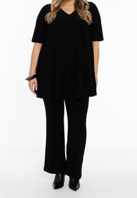 Zwarte tuniek met korte mouwen en een V-hals ontwerp, gecombineerd met zwarte wijde broek. Glad materiaal, minimalistische stijl en een getailleerde pasvorm.