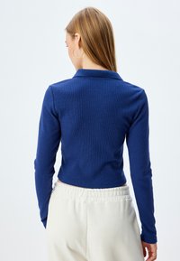 Polo a manica lunga di colore blu navy con un design aderente e una texture a coste; abbinato a pantaloni in maglia color crema con una vita elastica.