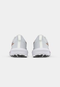 Witte sportieve schoenen met een gestructureerde bovenkant, voorzien van een gevoerde hiel tab, contrasterende gouden accenten en een zwarte rubberen zool met noppen.