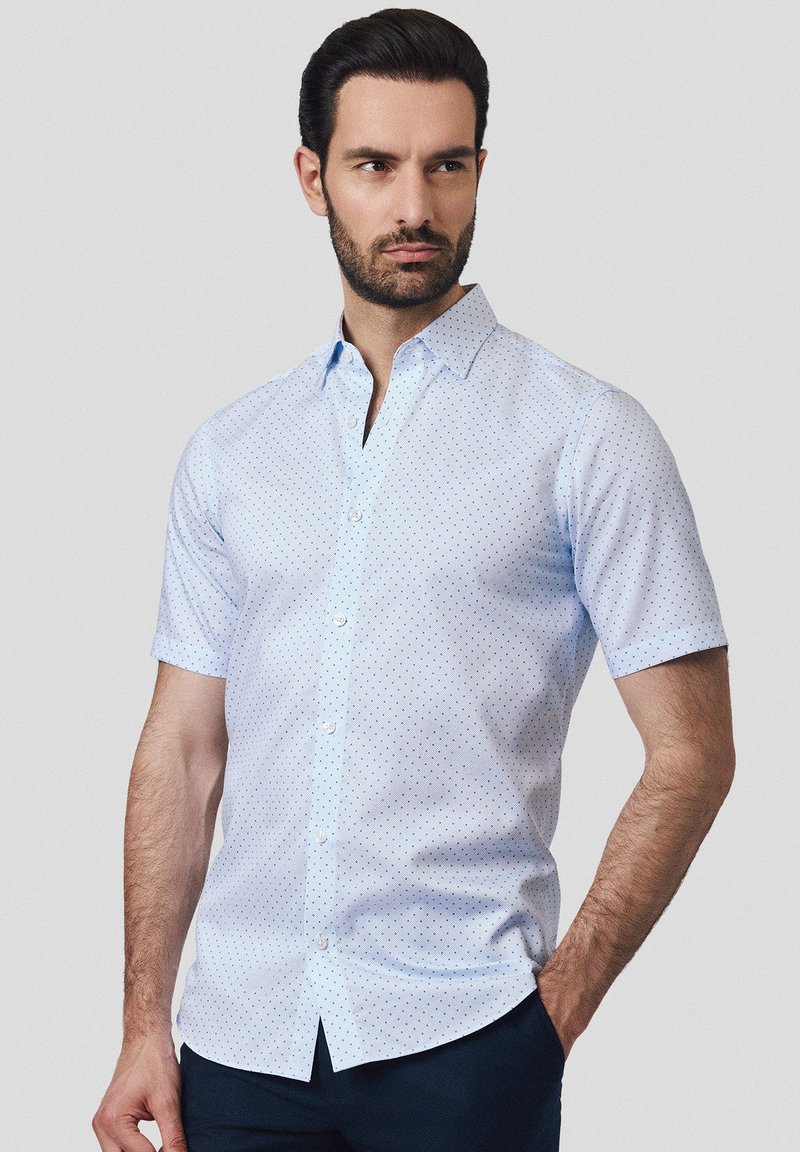 Koszula z krótkim rękawem w jasnoniebieskim kolorze w biały wzór w kropki. Posiada zapięcie na guziki z przodu oraz standardowy kołnierzyk.