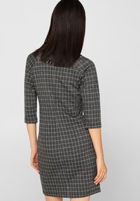 Musta-valkoinen ruudullinen mekko, jossa on kolme neljännesosaa hihat, istuva malli, sileä kangasrentous ja yksinkertainen helma.