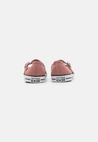 Zapatillas de lona rosas con suelas de goma blanca, que presentan un diseño clásico de caña alta, acentos de franjas negras y detalles del logo en el talón.
