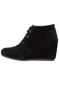 Stivali alla caviglia in suede nero con tacco a zeppa. Presentano lacci, dettagli cuciti e una texture liscia. Design minimalista con punta arrotondata.