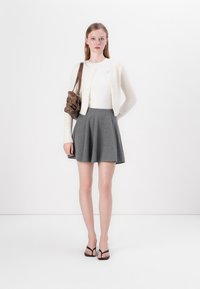 Cardigan blanc et duveteux sur un haut blanc ajusté, associé à une jupe grise évasée. Des tongs noires et un sac à main marron complètent le look.