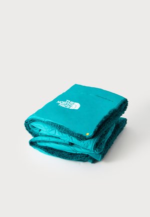Złożony turkusowy koc polarowy z puszystymi brzegami i białym logo The North Face na górze, prezentowany na białym tle.