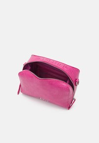 Růžová kabelka s krokodýlím vzorem a zapínáním na zip, vybavená vnitřní kapsou a tónovanou podšívkou. Elegantní logo je umístěno na přední straně.